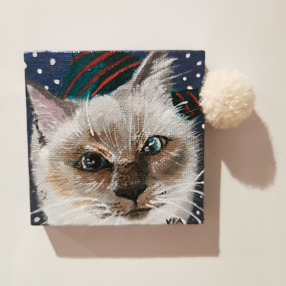 Le chat balinais avec son regard expressif et sa fourrure blanche sur un fond bleu enneigé et son bonnet de lutin a pompon